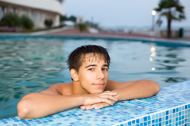 Teenager boy relaxing near ledge in pool open-air, looking at ca - Fotó, kép