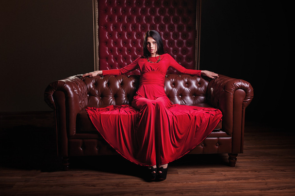 young woman in red dress sitting on leather sofa - Photo, Image