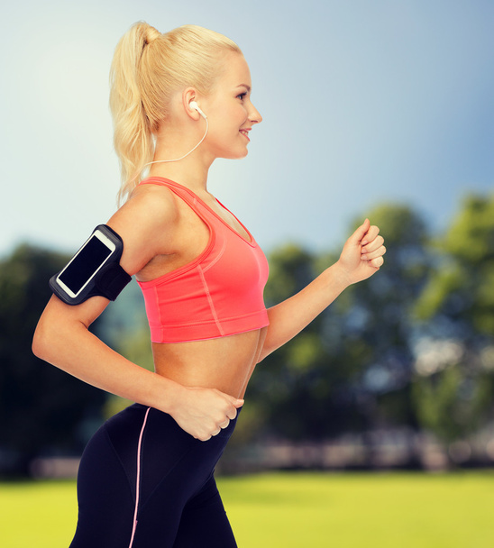 sporty woman running with smartphone and earphones - Photo, Image