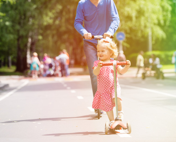 happy little girl and father on scooters in the city - Фото, изображение