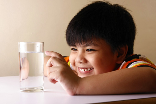 Niño tocando un vaso de agua en una mesa de madera
 - Foto, Imagen