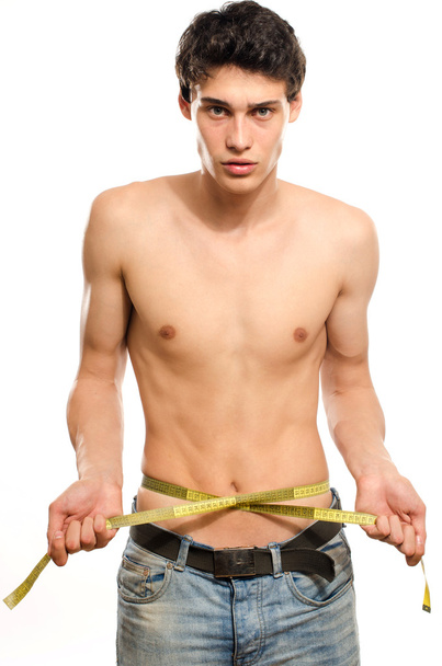 Skinny young man posing fashion with a centimeter, anorexic look. Slim body, young man keeping a strict diet and measuring himself - Photo, Image