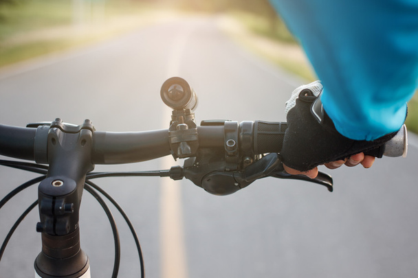 Hands in gloves holding handlebar of a bicycle on road. - Photo, Image
