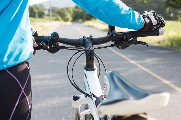 Manos en guantes sosteniendo el manillar de una bicicleta en la carretera
. - Foto, Imagen