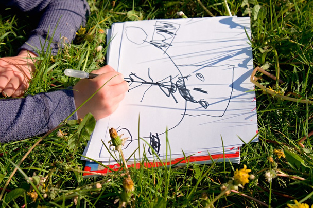 Vista cercana de la mano del niño dibujando adornos coloridos sobre papel. Cuaderno en hierba verde fresca del prado
. - Foto, imagen