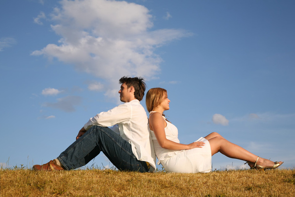 草原を背中合わせに座っているカップル - 写真・画像