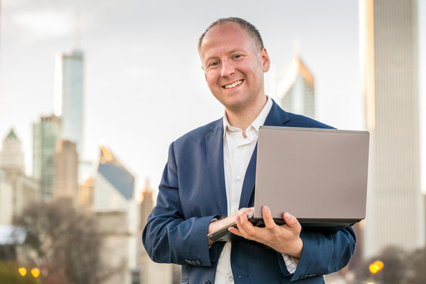 Бизнесмен с ноутбуком перед офисными зданиями
 - Фото, изображение