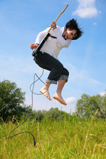 Young man jumps with guitar on grass - Φωτογραφία, εικόνα