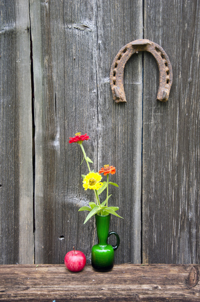 зелена скляна ваза з квітами, яблуком і підковою
 - Фото, зображення