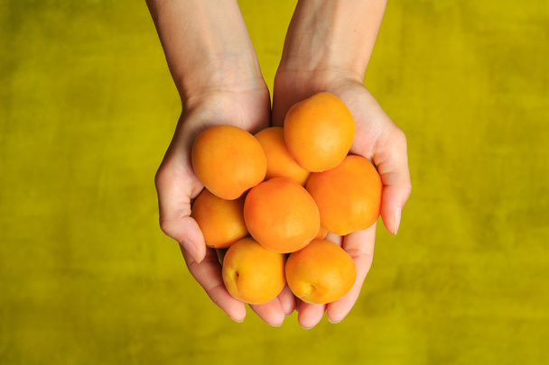 Yellow ripe apricots in woman's hands on green background - Foto, afbeelding