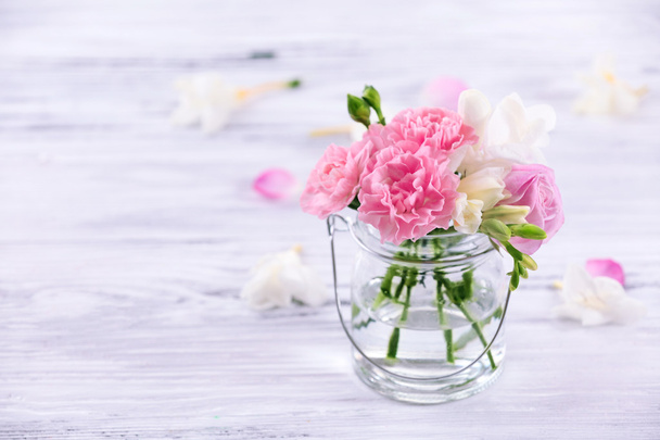 Beautiful spring flowers in glass bottle on wooden background - Photo, Image