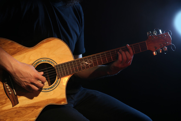 Young man playing on acoustic guitar on dark background - Fotografie, Obrázek