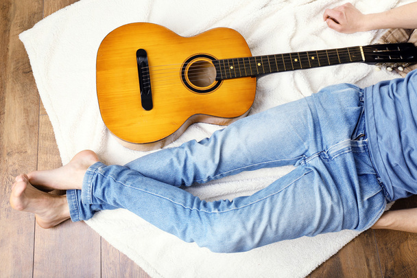 Young man with guitar on floor in room - Фото, зображення