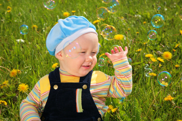 Child sits on grass and looks on soap bubbles - Foto, Imagem