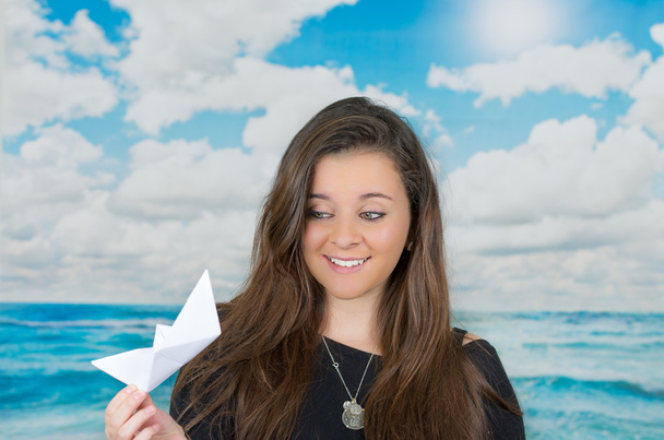 brunette holding an origami paper figure in front of oceanic cloud background - Foto, Imagen