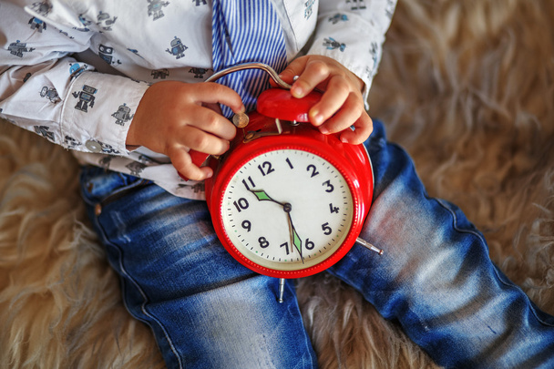 un niño pequeño sosteniendo un gran reloj rojo esperando milagros
 - Foto, imagen