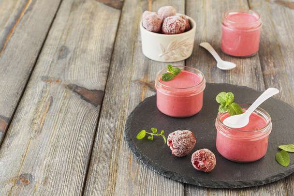 Strawberry mousse in glass jars and frozen strawberries on an old wooden table background.Selective focus. - Фото, зображення