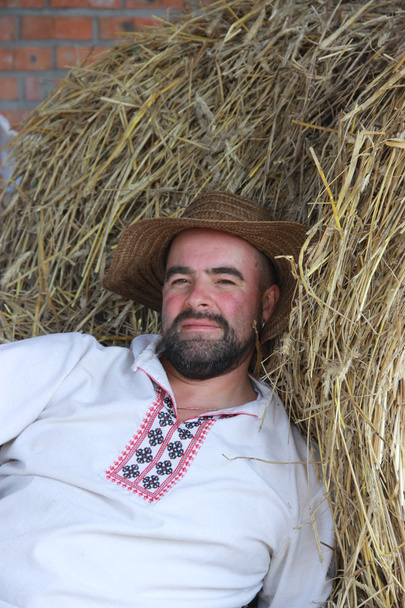 un hombre con una barba negra en una camisa blanca bordada yace cerca
  - Foto, Imagen