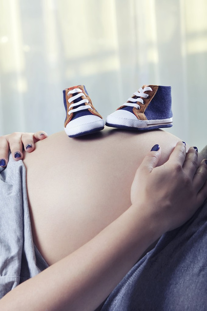 Small shoes for the unborn baby on the belly of pregnant woman - Foto, Imagen