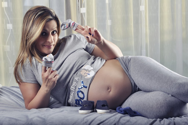 Happy future mommy showing her unborn baby boy socks - Foto, Imagen