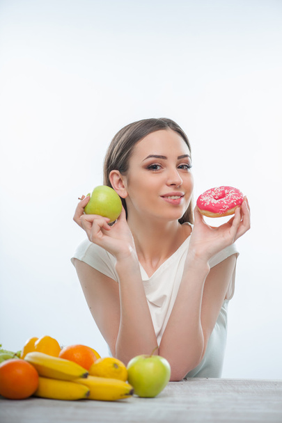 Beautiful young woman is sitting with healthy and unhealthy food - Foto, imagen