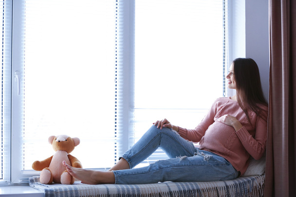 Pregnant woman sitting on windowsill background - Фото, изображение