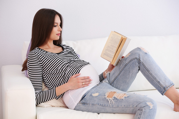 Pregnant woman with book on sofa in room - Zdjęcie, obraz
