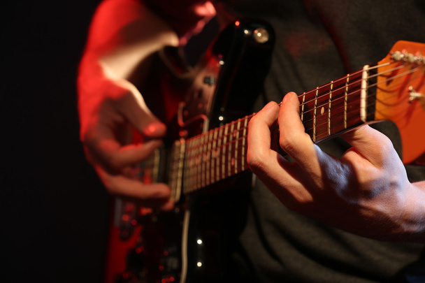 Young man playing on electric guitar on dark background - Foto, imagen
