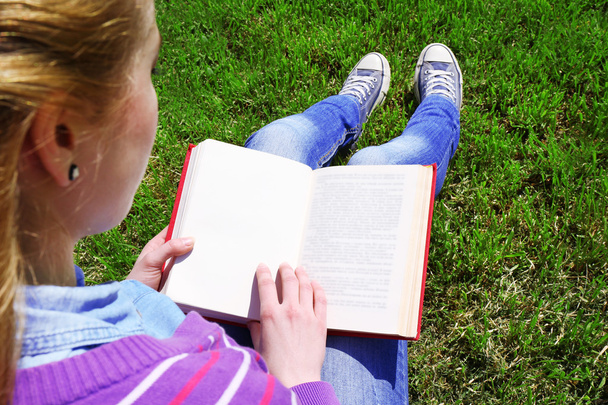 Young woman with book sitting on green grass outdoors - Фото, изображение