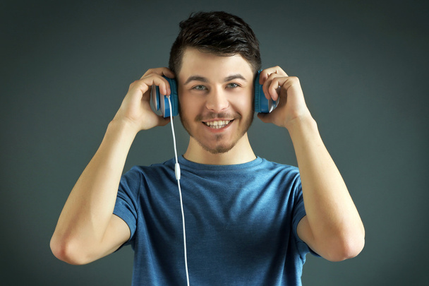 Handsome young man listening to music on grey background - Foto, imagen