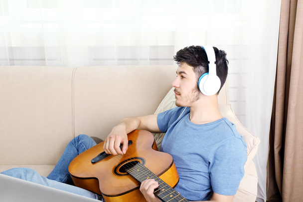 Young man with guitar on sofa - Zdjęcie, obraz