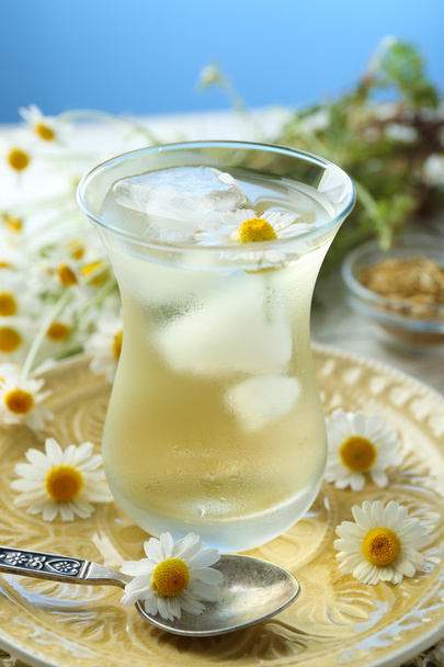Glass of cold chamomile tea with ice cubes and chamomile flowers on table, on colorful background - Zdjęcie, obraz