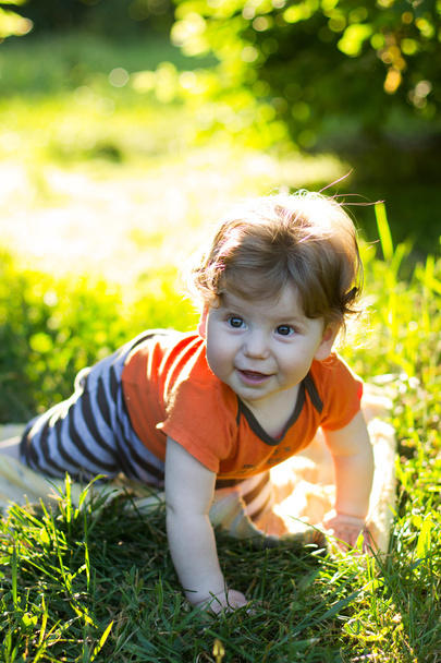 Красивый ребенок сидит в зеленой траве. Ребенок на улице. Дети ходят. Прогуляйся с ребенком. летний отдых
 - Фото, изображение