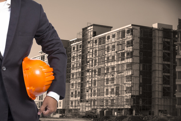 инженер держит оранжевый шлем для охраны рабочих на Контрукти
 - Фото, изображение