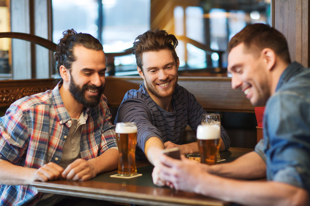 male friends with smartphone drinking beer at bar - Photo, image