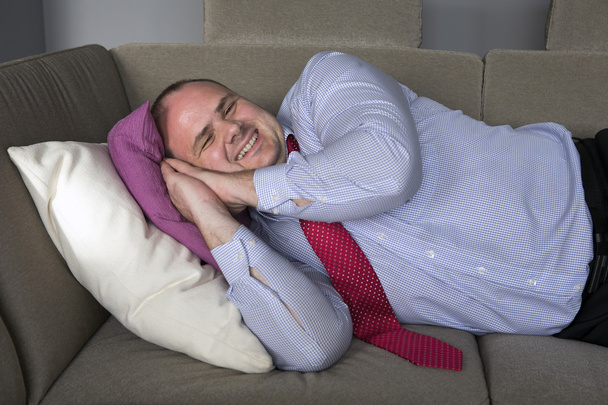 businessman lying on couch and smiles - Фото, изображение