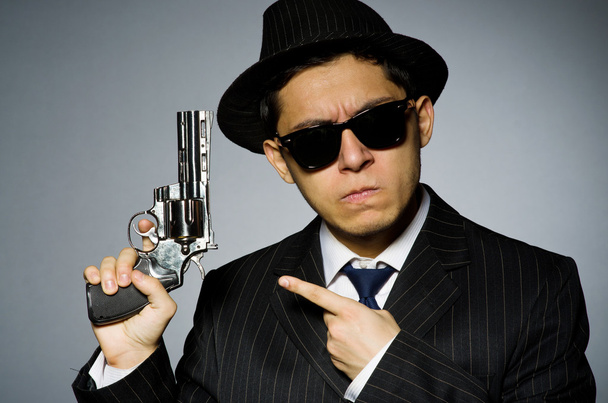 Młody człowiek w klasycznym pasiasty kostium trzymając pistolet na szarym tle - Zdjęcie, obraz