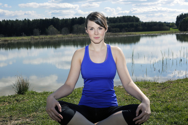 jovem mulher sentada junto a um lago em uma posição de lótus
 - Foto, Imagem