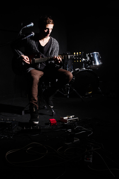 Mies soittaa kitaraa pimeässä huoneessa
 - Valokuva, kuva