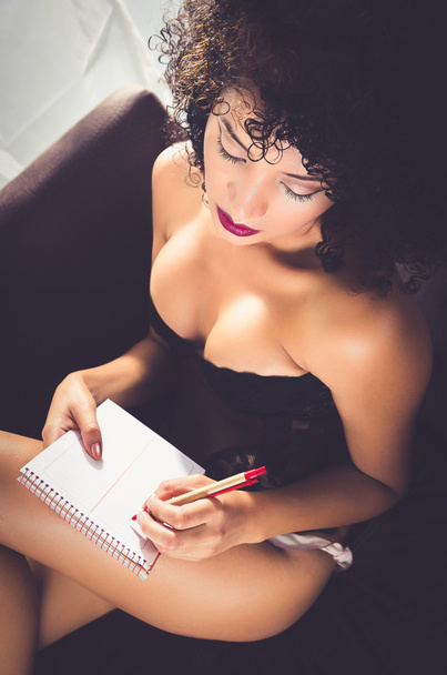 girl wearing lingerie sitting in sofa writing on paper - Фото, изображение