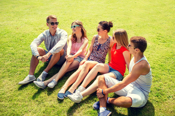 groep lachende vrienden buiten zitten in park - Foto, afbeelding