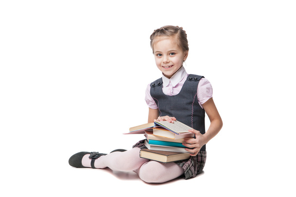 Beautiful little girl in school uniform with books sitting on the floor - Photo, image