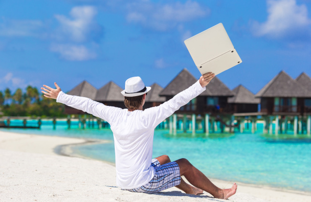 Jonge man met laptop genieten van vakantie in de buurt van water villa - Foto, afbeelding