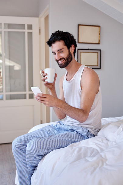 Man with cellphone and coffee on bed - Φωτογραφία, εικόνα