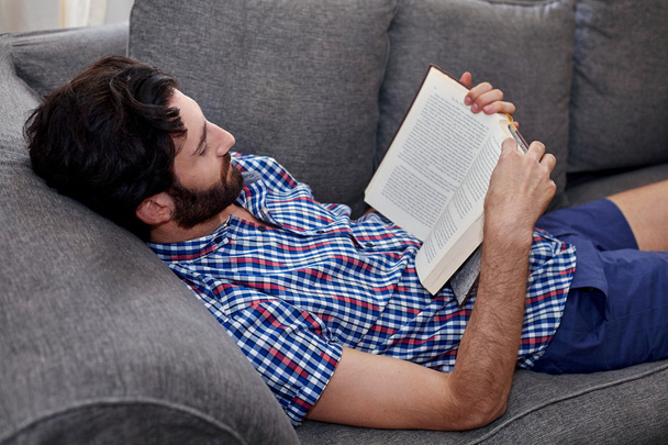 Man on sofa reading book at home - Foto, imagen