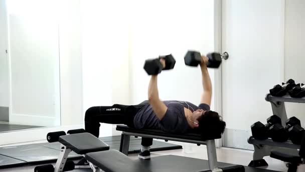 Ember emelésére az edzőteremben padon fekve súlyzók - Felvétel, videó