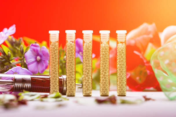 pequenos tubos de vidro com glóbulos homeopáticos, seringa e flores
 - Foto, Imagem