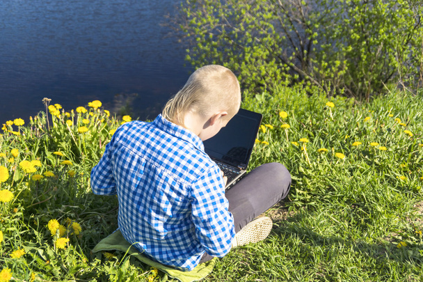 Ten year boy with laptop on riverside in summer - Foto, afbeelding