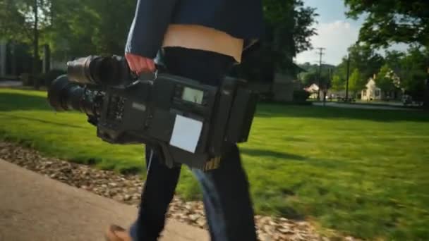 A low angle shot of a cameraman carrying his video camera to a production.  Trackable plane on camera for placement of a custom logo. - Footage, Video