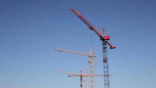 Крани працює на будівельному майданчику під ясне блакитне небо - Кадри, відео